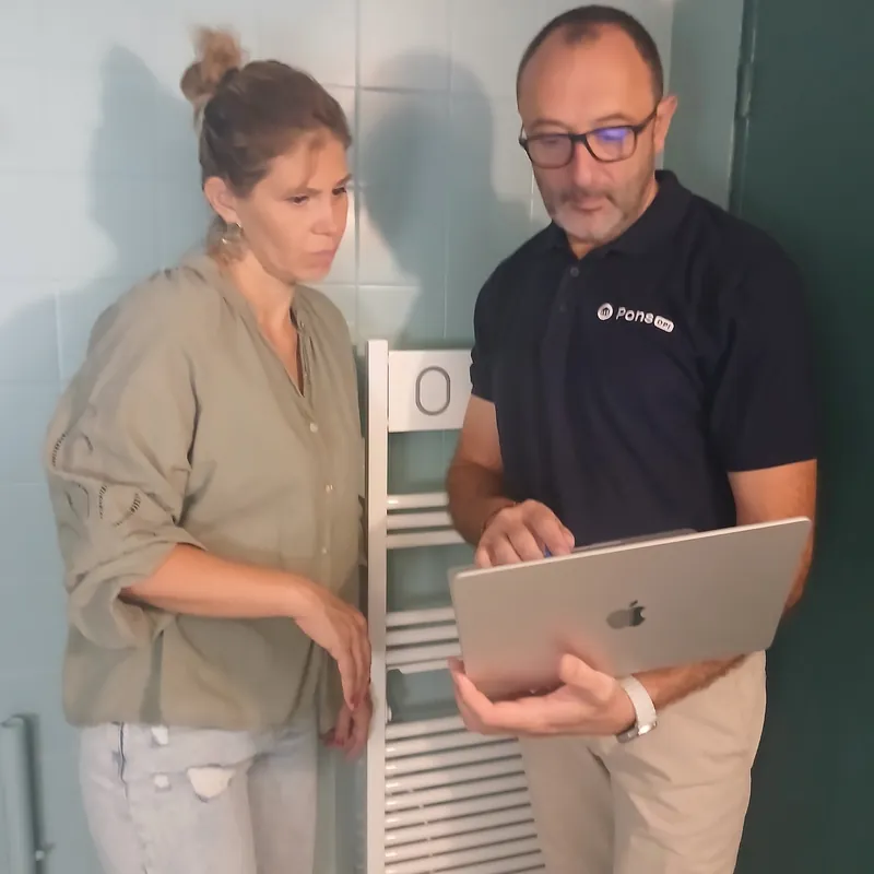 Guillaume Pons, ordinateur en main, examine un sèche-serviettes électrique avec la propriétaire