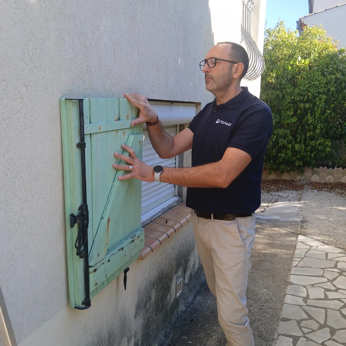 Guillaume Pons examine l’encadrement d’une fenêtre et ses volets en bois, en façade