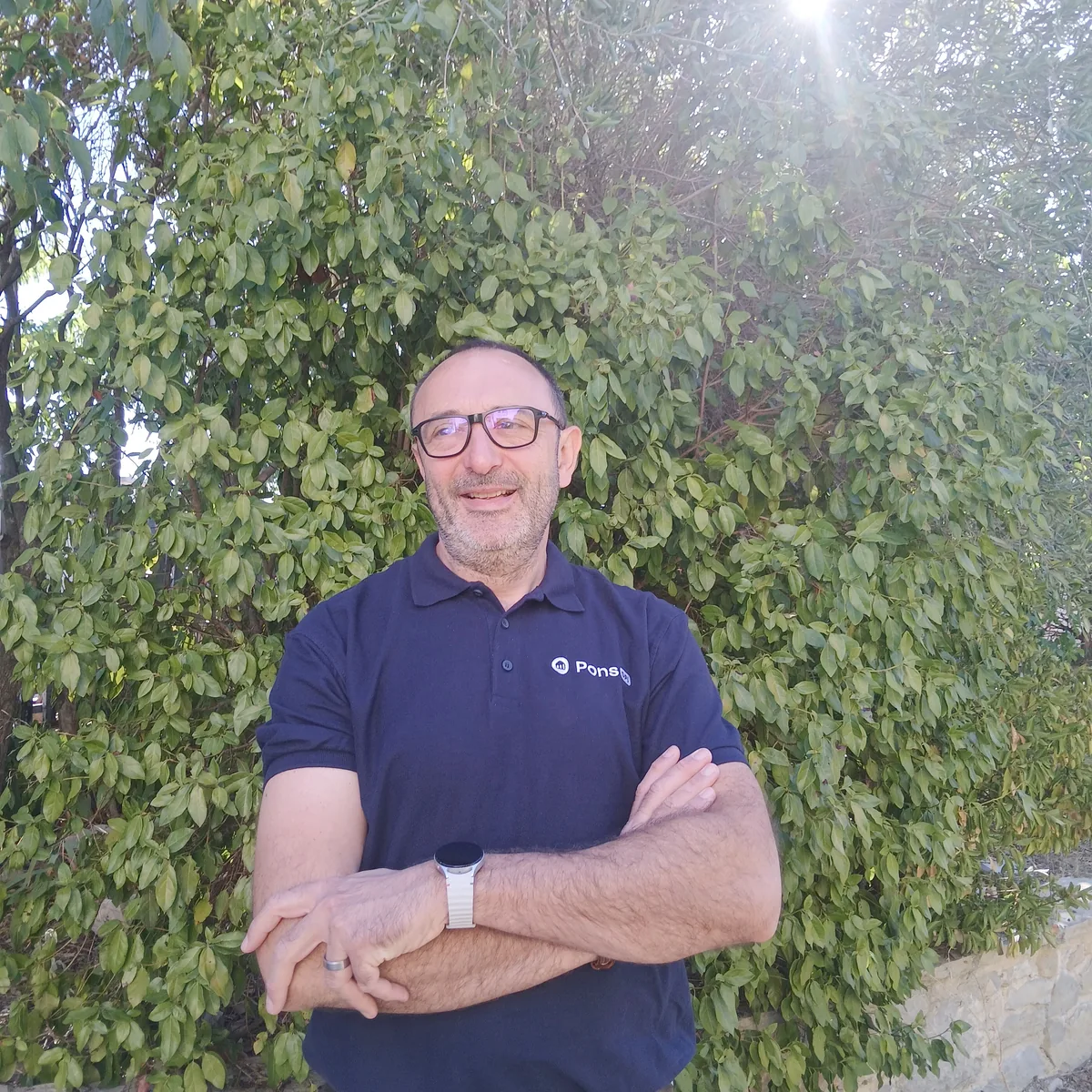 Guillaume Pons, souriant, bras croisés devant une haie