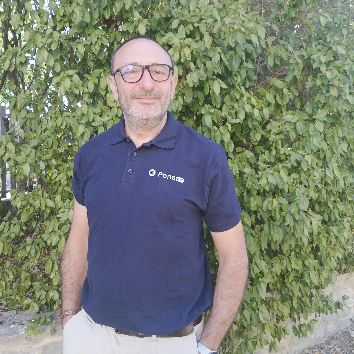 Guillaume Pons, souriant, les mains dans les poches, devant une haie